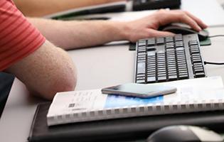 Computer keyboard, notepad, phone, and male hand on mouse